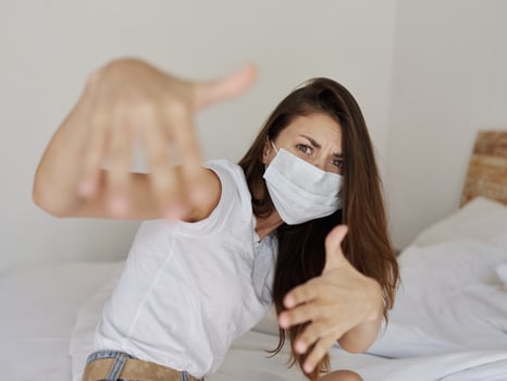 woman in medical mask gesturing with her hands while sitting on bed pandemic coronavirus vacation quarantine photo