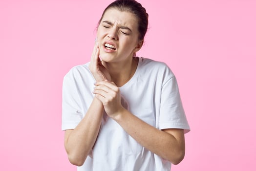 woman in white t-shirt holding her neck pain problems pink background photo