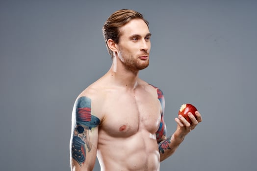sexy athlete with pumped up muscles eats an apple on a gray background and a tattoo on his arm photo