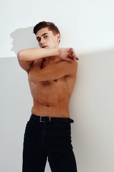 A man with a naked torso hugs himself with his arms on a light background and black pants model cropped view photo