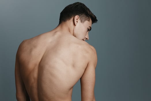 Sexy man with a naked back looks to the side against a gray background photo