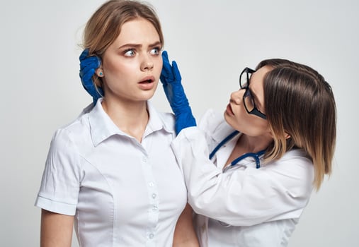 A woman doctor in a medical gown and blue gloves examines the patient's face photo