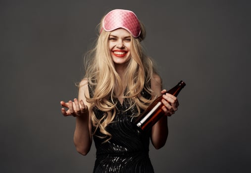 Woman with a bottle of beer on a gray background holidays sleep mask on her head photo
