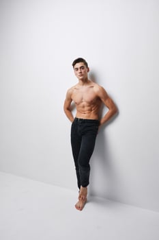A man with a naked torso sports figure pants light background room photo