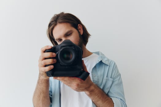 Man hipster photographer in a studio against a white background holding a professional camera and setting it up before shooting. Lifestyle work as a freelance photographer photo