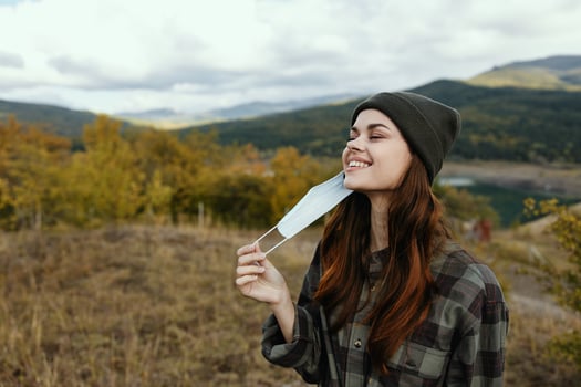 Modern woman in a medical mask smiles outdoors in the mountains in the forest photo