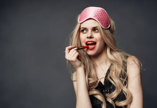 Drunk blonde with bright makeup on her face red lips and a pink sleep mask photo