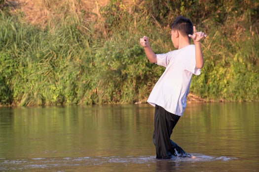 Asian boy is spending his freetimes by diving, swimming, throwing rocks and catching fish in the river happily, hobby and happiness of children concept, in motion. photo