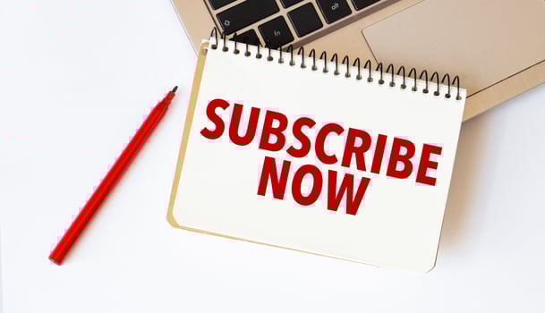 Laptop, red pen and notepad with text subscribe now in the white background photo