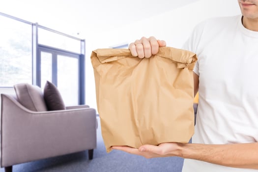 Young man holding paper bag, close-up. Wearing t-shirt, light grey background. Food delivery. photo