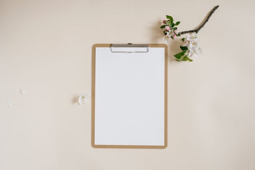 Blank sheet of paper with clipboard for tablet with copy space for copy. Beautiful home office table table workspace with fresh apple tree flowers. Flat lay, top view art concept photo