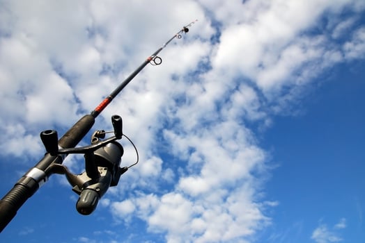 Spinning fishing rod against blue sky and clouds. Sport fishing, hobby, leisure and vacation photo