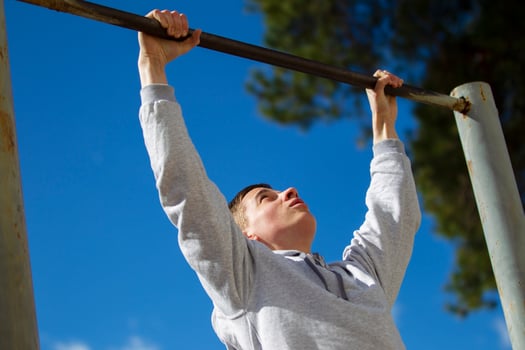 The boy pulls himself up on the horizontal bar on the street. A young man does exercises. photo
