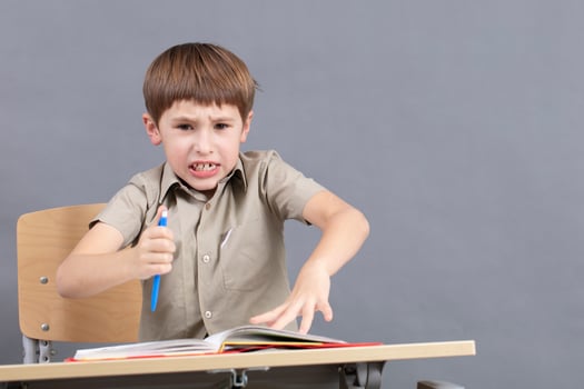 A primary school student is doing homework. The child at the desk with the textbook is angry. The boy does not want to study. A seven-year-old child goes crazy for lessons. photo
