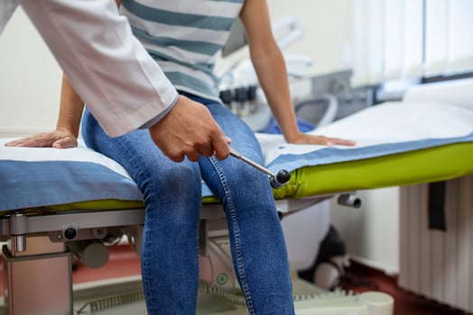 Doctor neurologist knocking on knee of patient with hammer in clinic closeup. Diagnosis of neurological pathology of knee reflex concept photo