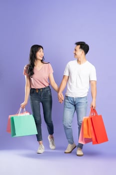 image of asian couple holding shopping bags on purple background photo