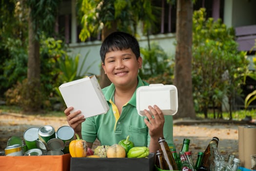 Asian boy is separating garbages and putting them into the boxes in front of him near building, soft and selective focus, environment care, community service and summer vacation activities concept. photo