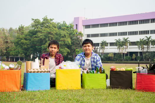 Asian boys are separating garbages and putting them into the boxes in front of them near building, soft and selective focus, environment care, community service and summer vacation activities concept. photo
