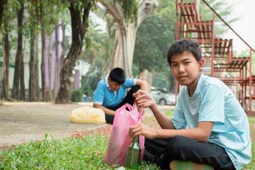 Young asian boy sorting various garbages and putting them into the boxes infront of him in the park, nature care and environment love concept. photo
