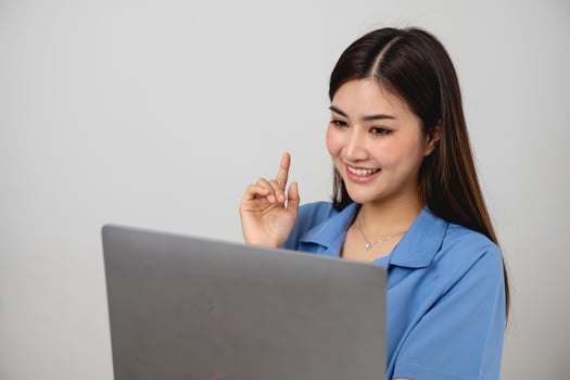 Young Asian woman with beautiful face, long hair in blue shirt sitting on white bedroom bed at home with cup of coffee and video call with laptop talking to relatives on holiday. vacation concept. photo