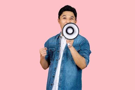 Happy asian man in casual shirt t-shirt scream in megaphone shout and showing triumph gesture on workspace isolated on pink  background. People lifestyle concept. photo