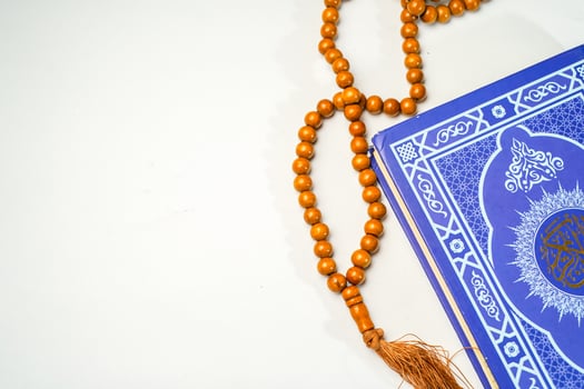 The Holy Al Quran with written arabic calligraphy meaning of Al Quran and rosary beads or tasbih on white background with copy space. photo