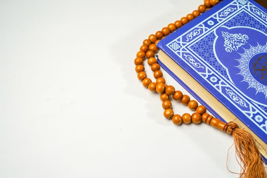 The Holy Al Quran with written arabic calligraphy meaning of Al Quran and rosary beads or tasbih on white background with copy space. photo