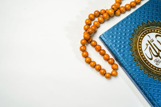 The Holy Al Quran with written arabic calligraphy meaning of Al Quran and rosary beads or tasbih on white background with copy space. photo