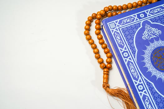 The Holy Al Quran with written arabic calligraphy meaning of Al Quran and rosary beads or tasbih on white background with copy space. photo