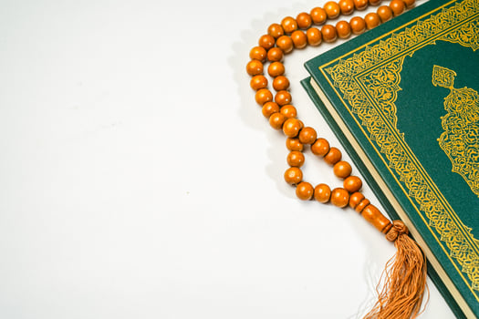 The Holy Al Quran with written arabic calligraphy meaning of Al Quran and rosary beads or tasbih on white background with copy space. photo