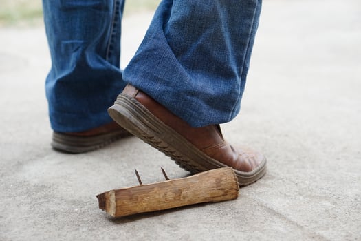 Closeup man wears shoes is stepping on rusty metal nail on wood. Concept, unsafe , risk for dangerous tetanus. Be careful and look around during walking at construction site or risk places. photo