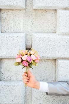 Groom holding a bouquet of pink rose flowers and concrete wall background. Valentine Day for love and celebration Concept. photo
