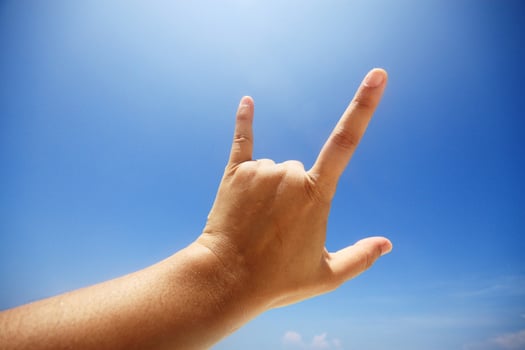 Hand sign of love and showing fingers means I love you on blue sky with sunlight and copty space. photo