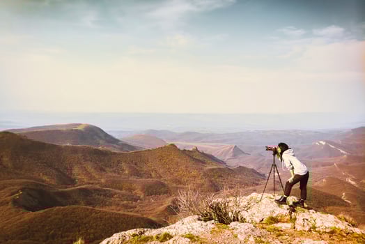 Young passionate attractive caucasian hipster woman content creator photographing mountains with red girly DSLR camera on tripod photo