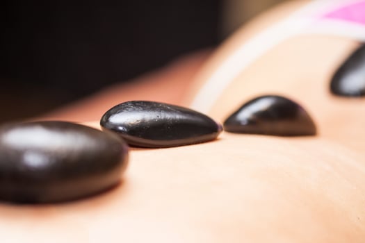 Doctor performing a hot volcanic stones therapy on a young female patient back photo