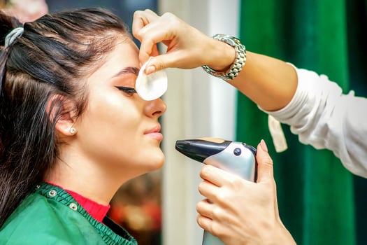 Side view of a make-up artist using aerograph making an airbrush makeup foundation on a female face in a beauty salon. photo