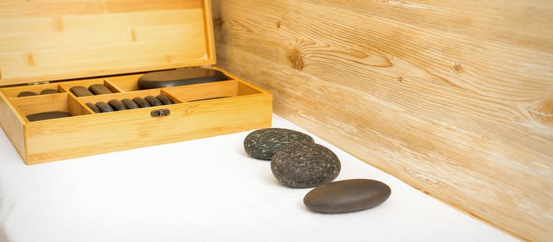 Black massage stones lying near the wooden box with massage rocks on the towel on the table. photo