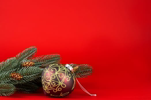 christmas card. Green branches of a christmas tree with cones and a Christmas ball with gold ornaments on a red background photo