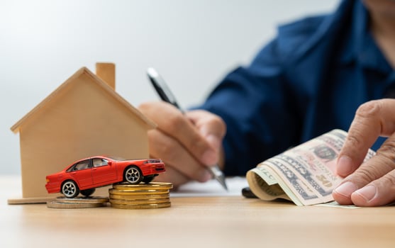 Unhappy Asian man holding a banknote and Making an account of income and expenses to pay the home loan and car loan, Concept loan payment and home insurance, economic problems, and inflation photo
