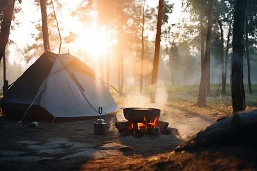 A tent in the forest in the summer by a fire with a pot from which steam comes from food. . photo