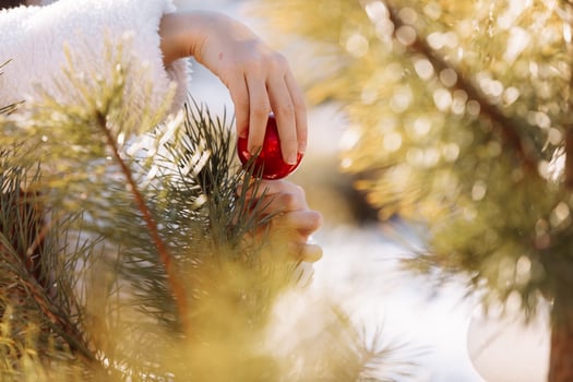 Child girl is decorating Christmas tree with shiny white and red balls outdoors before the holidays. Kid in warm jacket is having fun in park in winter day. Merry Xmas and happy family holidays photo