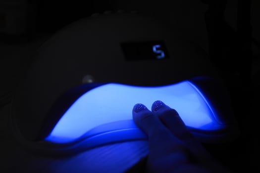 Closeup view of female hands with gel polish manicure. Woman puts hand into led uv lamp for curing top cover of nailpolish. UV lamp, LED Nail photo