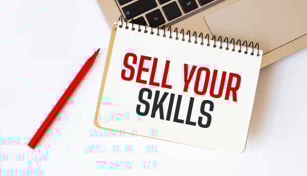 Laptop, red pen and notepad with text sell your skills in the white background photo