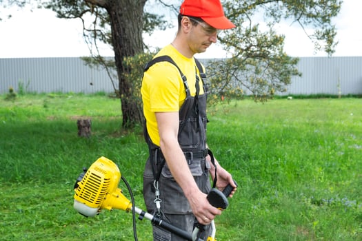 A male gardener mows the green grass of the lawn in the backyard with a gasoline mower. Trimmer for the care of a garden plot photo