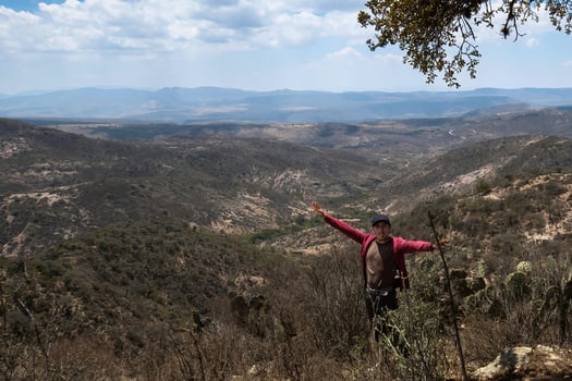Man stands on a hill with his arms outstretched in the air, with a view of mountains in the distance. photo