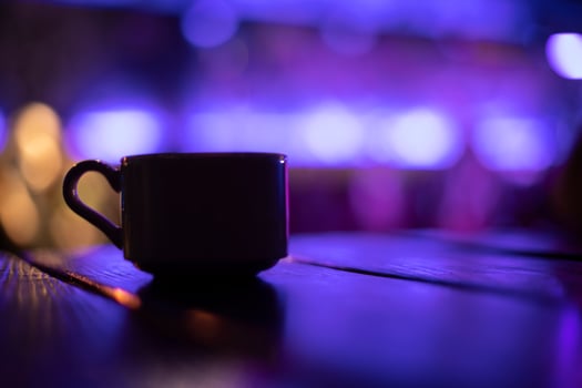 Cup on table in purple. Silhouette of cup in dark room. Mug with drink. photo