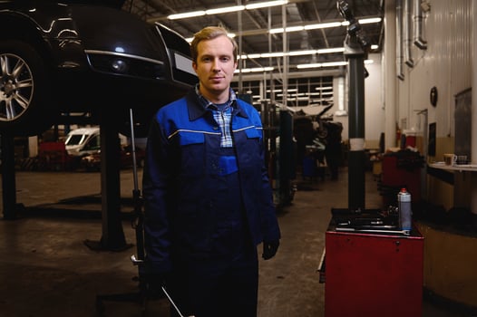 A technician, auto mechanic, car engineer standing against the background of a lifted automobile with wrench in his hand, working in repair shop or car service garage photo