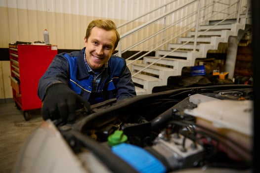 Handsome young Caucasian car engineer, technician mechanic in car service adjusting headlights on car in the repair shop garage. Auto service, car repair and warranty maintenance concept photo