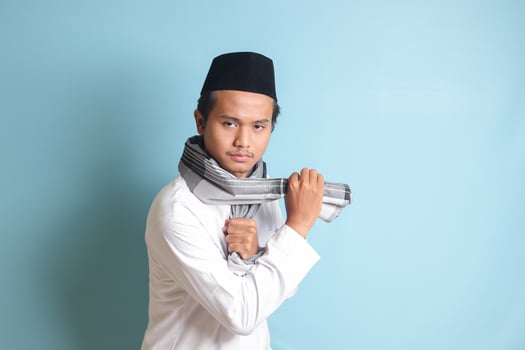Portrait of Asian muslim man in white koko shirt doing martial arts gesture or pencak silat. Isolated image on blue background photo