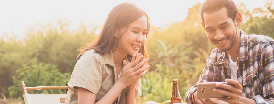 Happy, Cheerful asian young woman, girl and man holding, using smartphone sitting on chair outside tent. Adventure couple love camping in forest. Eco activity, lifestyle nature on holiday concept. photo